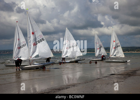 Beached White Barche a vela, yacht laser in mare, dingies e rimorchi a Marazion, vicino al Monte di San Michele, Penzance in Cornovaglia. Foto Stock