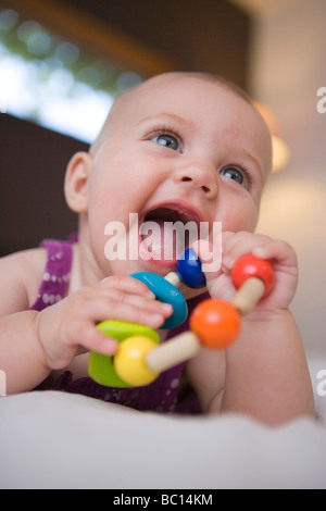 Baby ragazza sorridente e tenendo un legno giocattolo per la dentizione con la bocca aperta Foto Stock