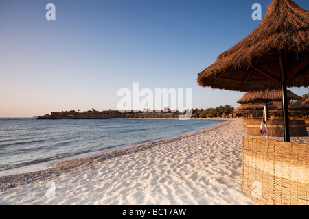 Con il tetto di paglia ombrelloni e frangivento su una spiaggia deserta Foto Stock