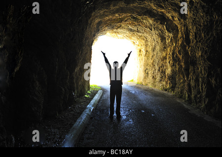 La luce alla fine del tunnel. Silhouette di una figura in piedi alla fine di un tunnel buio guardando fuori in presenza di luce solare intensa. Foto Stock