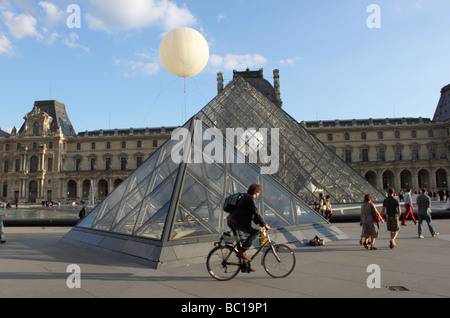 Giovane uomo cicli nella parte anteriore della piramide di vetro al Louvre di Parigi Foto Stock