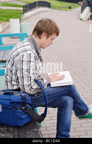 Ragazzo con libro siede sulla città una panchina nel parco Foto Stock