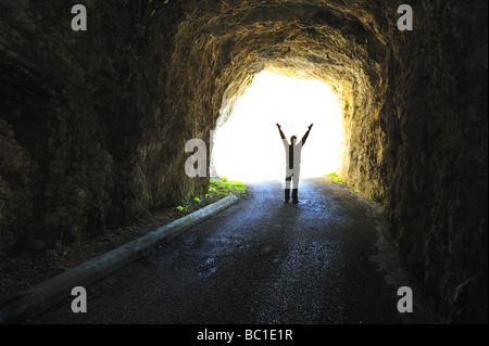 La luce alla fine del tunnel. Silhouette di una figura in piedi alla fine di un tunnel buio guardando fuori in presenza di luce solare intensa. Foto Stock