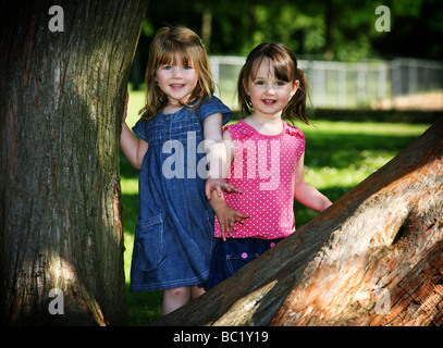 Due 3 anno di età pre-scuola bambini ragazza migliori amici a giocare insieme con gli alberi nel parco locale sorridente ridendo estate all'aperto Foto Stock