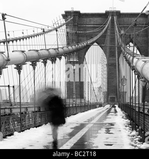 Pedestirian con ombrellone passando sul ponte di Brooklyn Foto Stock