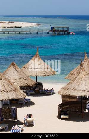 I vacanzieri su un egiziano Beach con un molo di immersioni in distanza al di sopra del mare rosso Foto Stock
