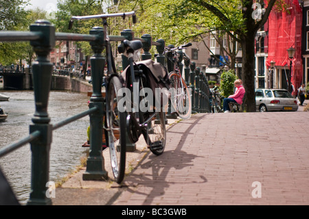 Bicicletta parcheggiata contro una ringhiera in ferro su un ponte su un canale in Amsterdam Foto Stock