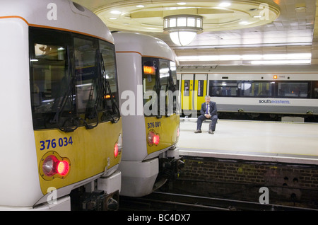 Un " commuter " si siede in attesa di un treno, stazione ferroviaria di Charing Cross, London REGNO UNITO Foto Stock