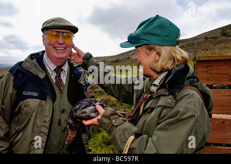 Donna di applicare il sangue alla guancia del tiratore dopo che egli ha ucciso il suo primo Red Grouse durante riprese nelle Highlands della Scozia Foto Stock