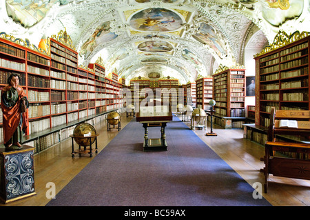 PRAGA, Repubblica Ceca: Gli interni ornati della Biblioteca Strahov, parte del monastero Strahov di Praga. Sulla sinistra si trova la statua di San Giovanni Evangelista, mentre sulla destra si trova una ruota del libro appositamente progettata, un'innovativa invenzione rinascimentale che consente ai lettori di fare riferimento a più libri contemporaneamente ruotando la ruota. L'elaborato arredamento barocco della biblioteca, compresi soffitti affrescati e scaffali dorati, mostra il suo significato come deposito di conoscenza e patrimonio culturale. Foto Stock