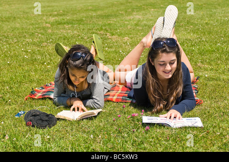 Ritratto orizzontale di due attraenti ragazze giovani sdraiati sull'erba libri di lettura e ascolto di un ipod in una giornata di sole Foto Stock