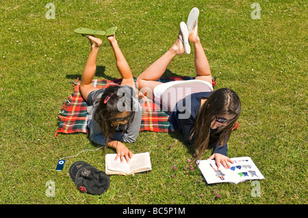 Antenna orizzontale ritratto di due attraenti ragazze giovani sdraiati sull'erba libri di lettura e ascolto di un ipod al sole Foto Stock