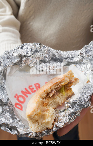 Persona in possesso di Döner Kebab, parzialmente consumato, in lamina di alluminio - Foto Stock