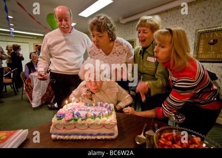 Assistito da familiari e amici un centenario si brucia le candele sulla sua torta durante il suo centesimo compleanno Foto Stock