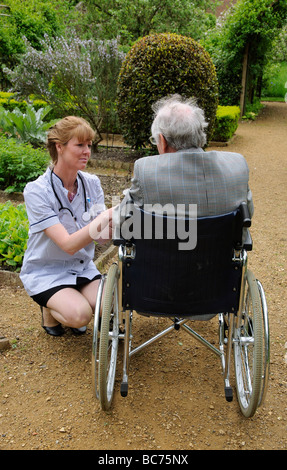 Infermiere caregiver frequentando il maschio anziano un paziente su una sedia a rotelle Foto Stock