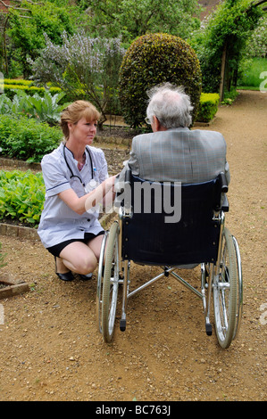 Infermiere caregiver frequentando il maschio anziano un paziente su una sedia a rotelle Foto Stock