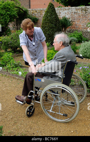 Infermiere caregiver frequentando il maschio anziano un paziente su una sedia a rotelle Foto Stock