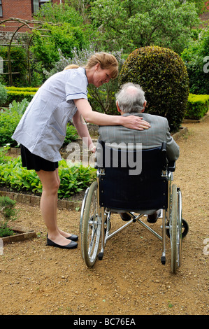 Infermiere caregiver frequentando il maschio anziano un paziente su una sedia a rotelle Foto Stock