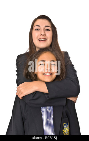 Chiudere verticale su ritratto di due sorelle adolescenti nelle loro uniformi di scuola che abbraccia ogni altra contro uno sfondo bianco Foto Stock