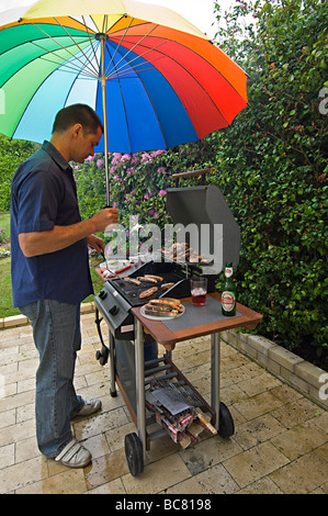 Verticale umoristico ampio angolo di un uomo in piedi la cottura su un barbeque sotto la pioggia su una tipica wet British giorno d'estate Foto Stock