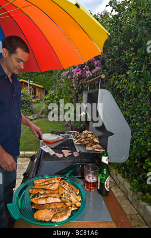 Verticale umoristico ampio angolo di un uomo in piedi la cottura su un barbeque sotto la pioggia su una tipica wet British giorno d'estate Foto Stock