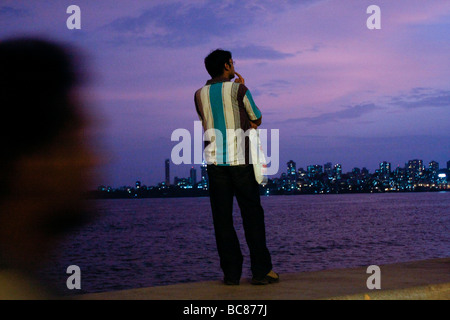 Un uomo indiano con una borsa per la spesa si affaccia sul mare da Marina Drive in Mumbai in India Foto Stock