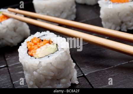 Un inclinato orizzontale poco profonda focus macro di sushi con copsticks su un nero lo sfondo di legno Foto Stock