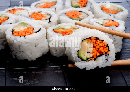 Bacchette azienda sushi infront di più un sushi nero testurizzato sfondo Foto Stock