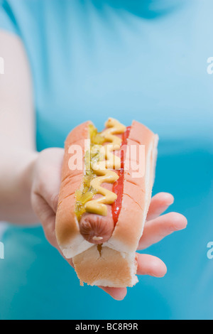 Donna che mantiene un hot dog con senape, sottaceti e ketchup - Foto Stock