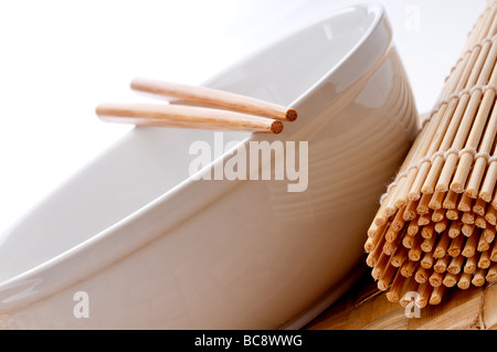Un inclinato immagine orizzontale di un paio di bacchette su una vaschetta di colore bianco con un rotolamento suhi tappetino su un intessute placemat Foto Stock