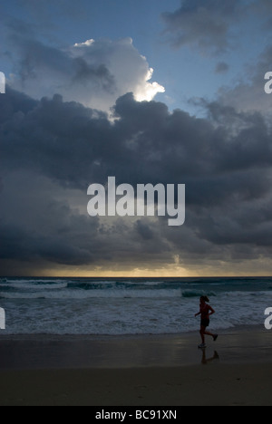 Donna in corsa sulla spiaggia, la mattina presto, sub tropicale nuvole temporalesche, Burleigh teste, Surfers Paradise, Queensland, Australia Foto Stock
