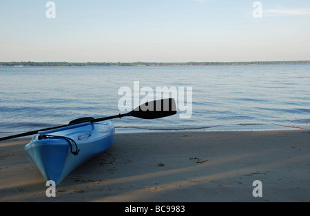 Blue kayak spiaggiata accanto a un ampio fiume blu sotto un cielo blu. Foto Stock