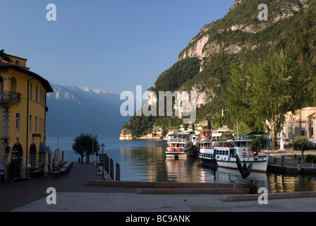 Vista di mattina presto su Piazza III Novembre fino ai traghetti sul lago e sulle montagne di Riva del Garda sul Lago di Garda Foto Stock