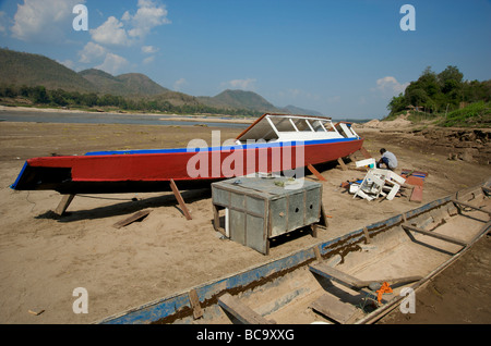 Una barca del fiume Mekong che ottiene un lick di vernice dal suo proprietario sulle rive del fiume Mekong in Luang Prabang Laos Foto Stock