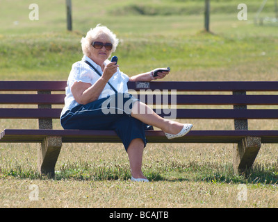 Vecchia donna seduto su una panchina nel parco texting Foto Stock