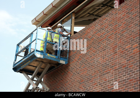 Gli uomini utilizzando una piattaforma per l'installazione di Windows in un edificio di nuova costruzione Foto Stock