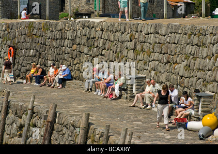 Turisti che si godono il sole sulla parete del porto Clovelly North Devon England Foto Stock