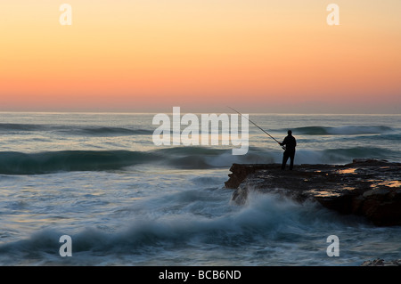 Un pescatore sull'oceano rocce all'alba Foto Stock