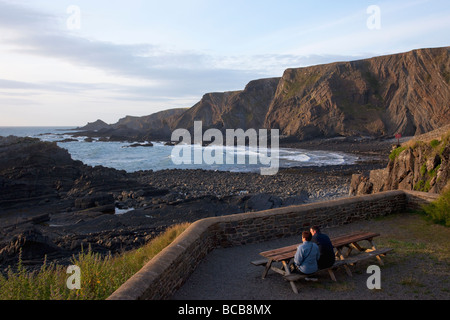 Coppia giovane ammirare vista bere birra giardino Hartland Quay sentiero costiero North Devon Heritage Coast Inghilterra Regno Unito Regno Unito Foto Stock