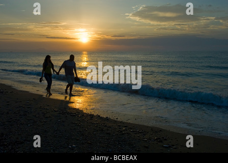 L uomo e la donna a piedi lungo una spiaggia tenendo le mani al tramonto Foto Stock
