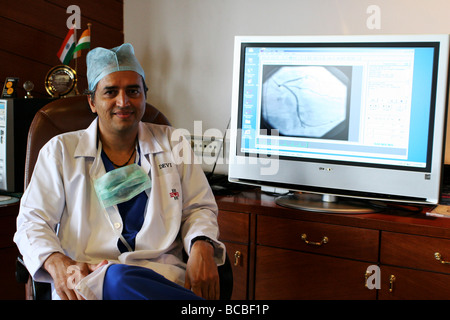 Il dr. Devi Shetty si siede di fronte a un monitor ad alta definizione che mostra parte di un paziente. Questo è un esempio di telemedicina. Foto Stock