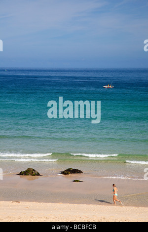 Giovane donna femmina del jogging jogging sulla spiaggia Porthmeor con barca da pesca in estate St Ives Cornwall Inghilterra UK Regno Unito GB Foto Stock