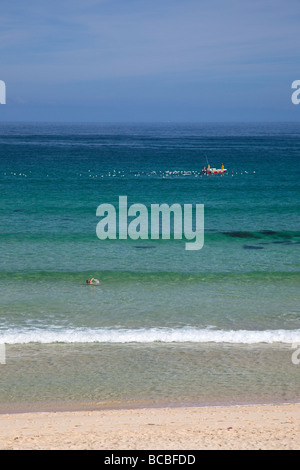 Giovane donna femmina a nuotare in mare al largo Porthmeor beach con barca da pesca in estate St Ives Cornwall Inghilterra UK Regno Unito GB Foto Stock