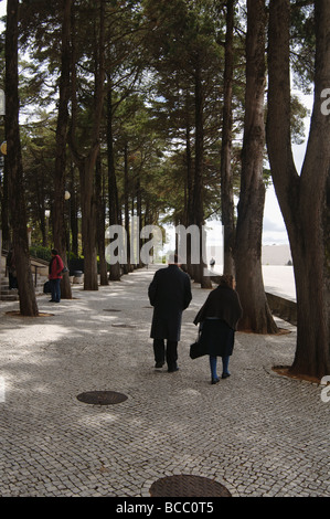 Senior tradizionale coppia sposata vestita di nero camminando per strada alberata Foto Stock