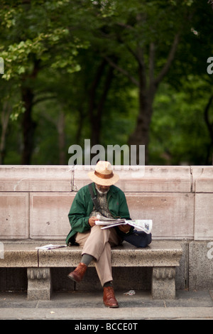 Uomo nero si siede su un banco di pietra da un parco e si legge il giornale in New York USA Maggio 2009 Foto Stock