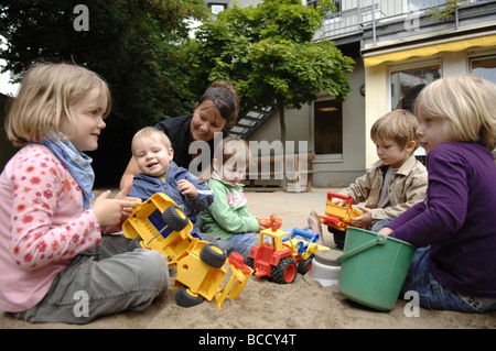 I bambini e il maestro giocando su un parco giochi in un asilo nido su un giorno d'estate. Foto Stock