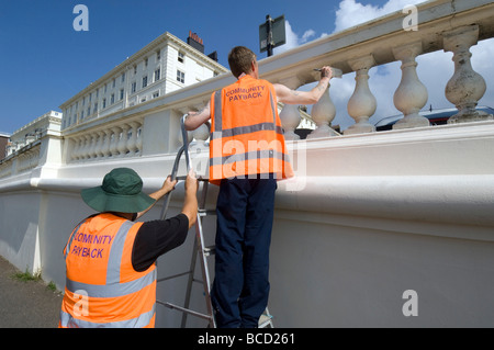 I criminali condannati a fare pittura e decorazione in arancione tabards con comunità payback slogan sul retro Foto Stock