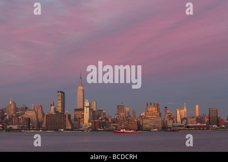 Il sole al tramonto proietta un bagliore di magenta sul cielo sopra l'Empire State Building e lo skyline di Manhattan come visto dal New Jersey. Foto Stock