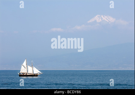 Una goletta a vela sull'Oceano Pacifico passa lentamente davanti a un Monte Fuji parzialmente oscurato vicino a Numazu, in Giappone Foto Stock