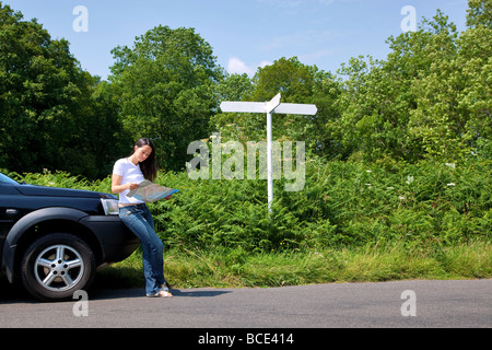 Una donna appoggiata al suo auto come lei legge una mappa accanto a un cartello stradale il segno è vuota per aggiungere il proprio testo Foto Stock